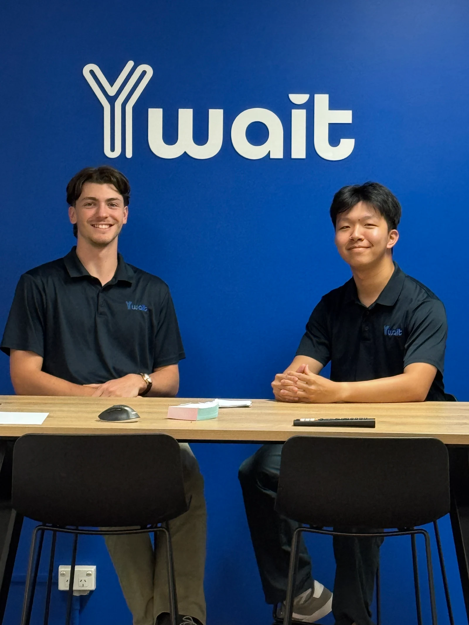 Two Ywait team members seated together beneath the Ywait logo